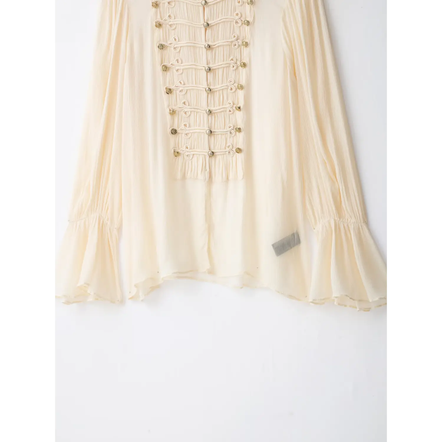 Lower hem view of cream textured chiffon blouse, bell long sleeves, flat background