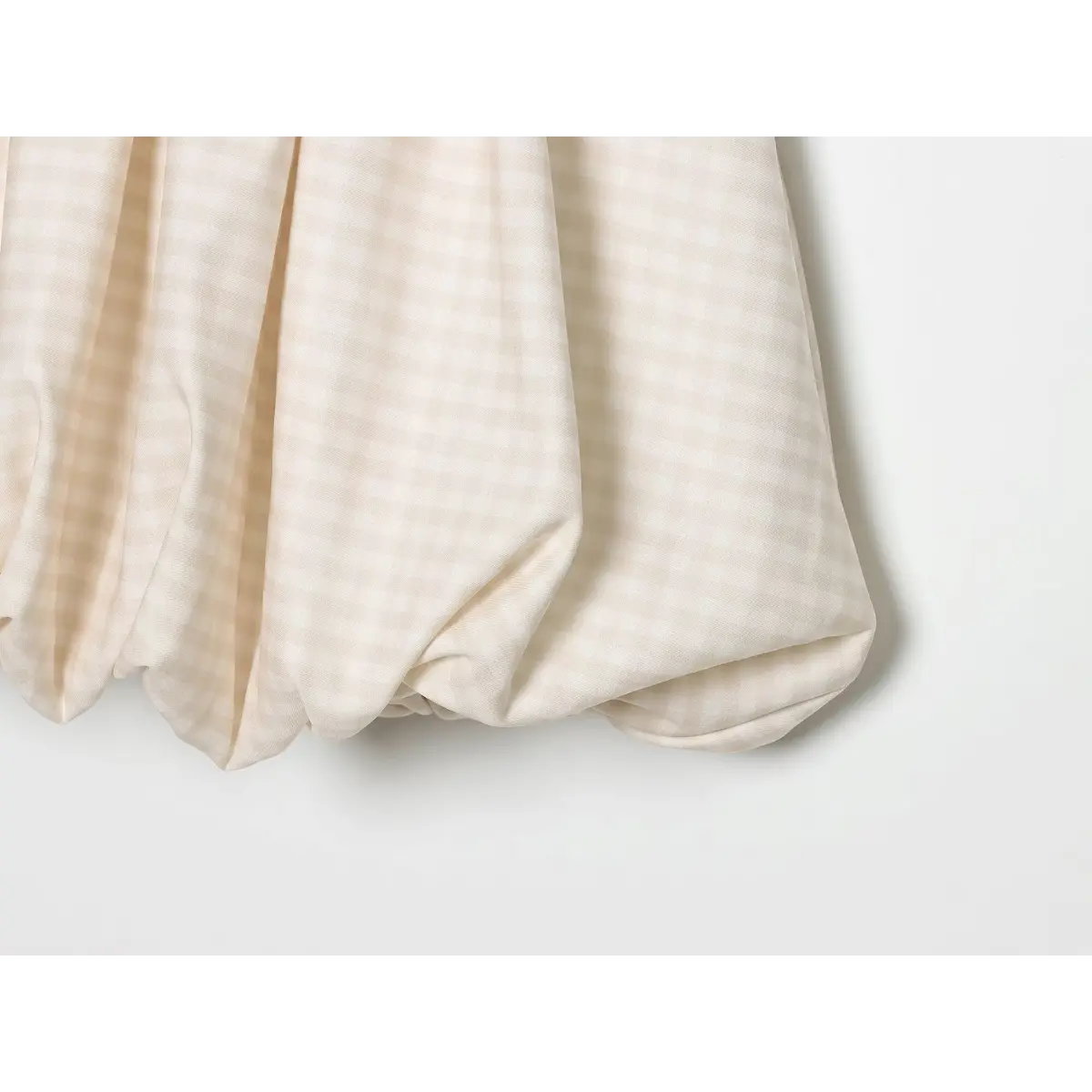 Close-up of the puffed bubble hem and gingham fabric texture on the cream cami dress