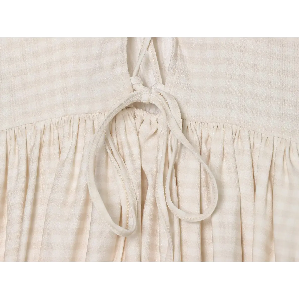 Close-up of the front tie detail and gathered skirt construction on the cream gingham cami dress
