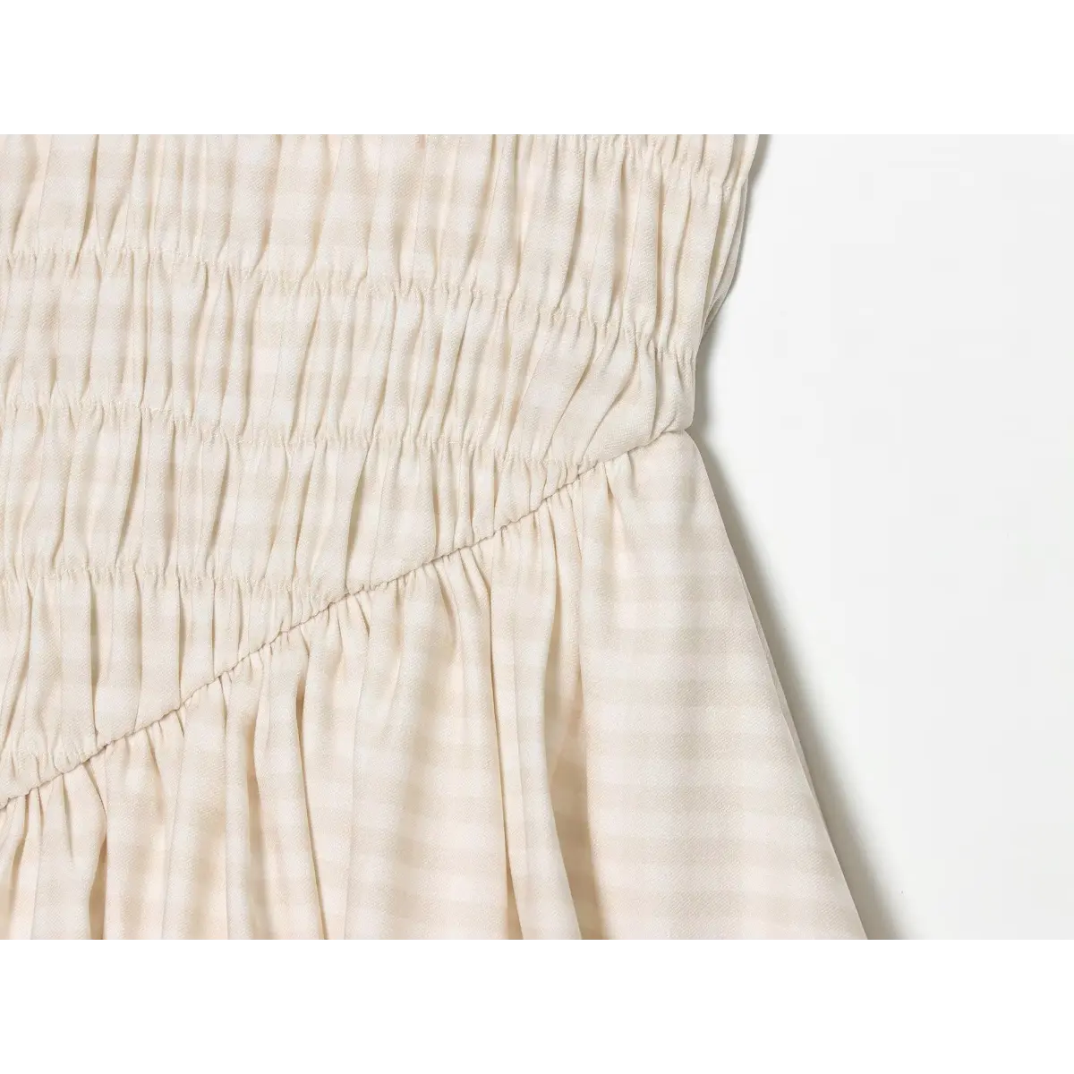 Close-up of the diagonal seam and smocked waist detail on the cream gingham cami dress