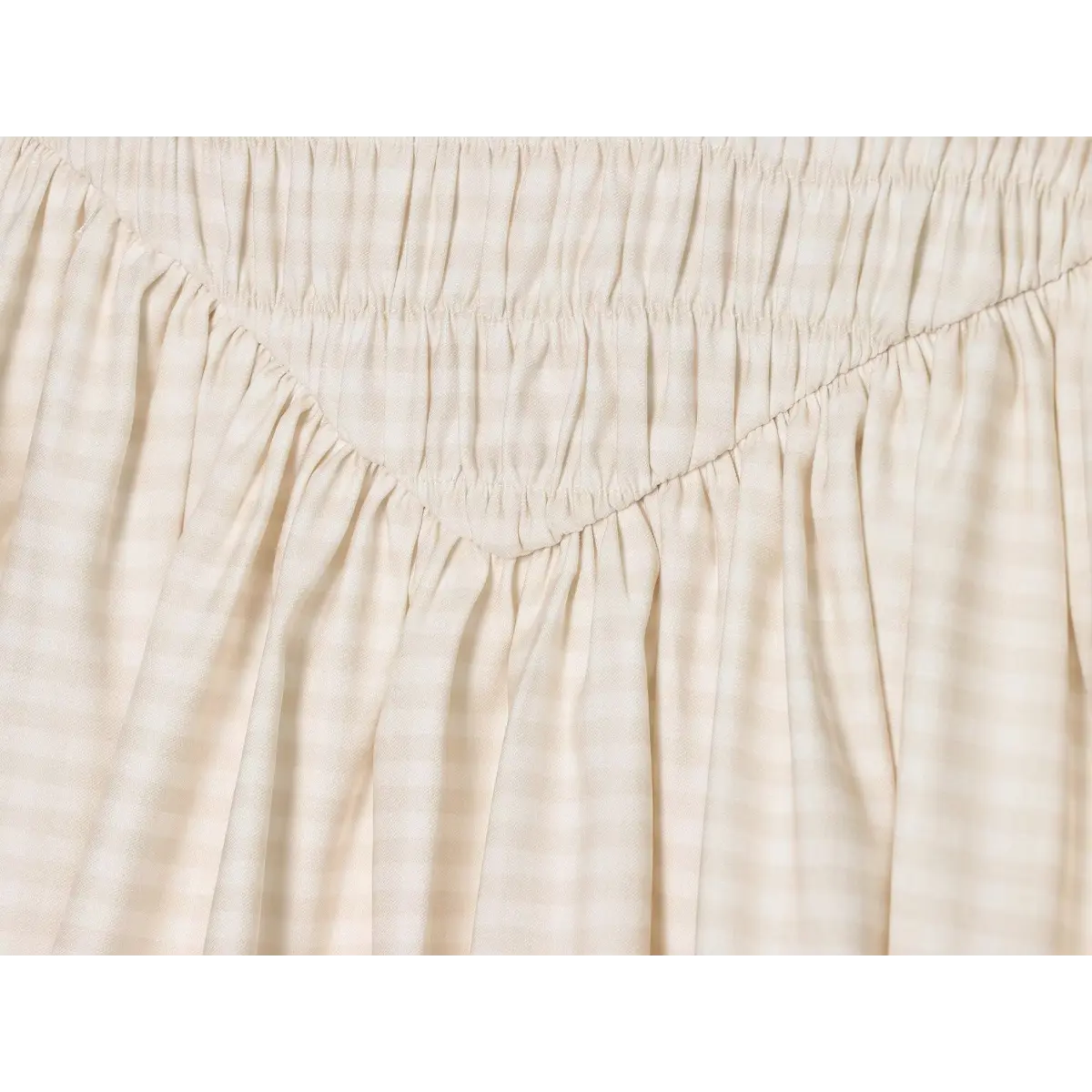 Close-up of the smocked waistband and gathered fabric on the cream gingham cami dress