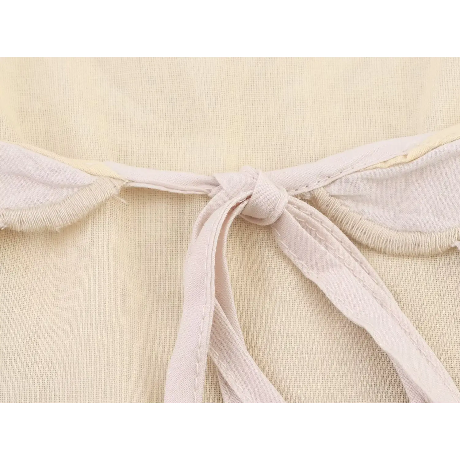 Close‑up shot of fabric tie knot at halter neck on cream embroidered halter top