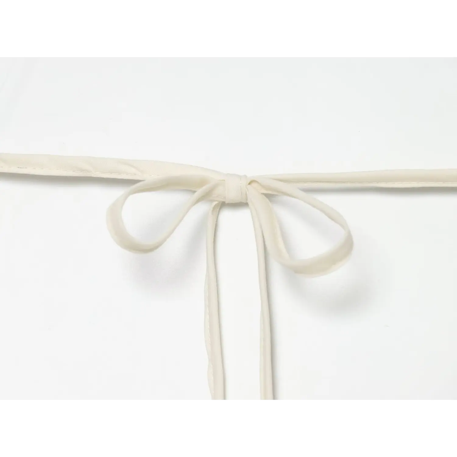 Extreme close‑up of fabric tie bow for halter back closure, fine stitching detail on cream dress strap