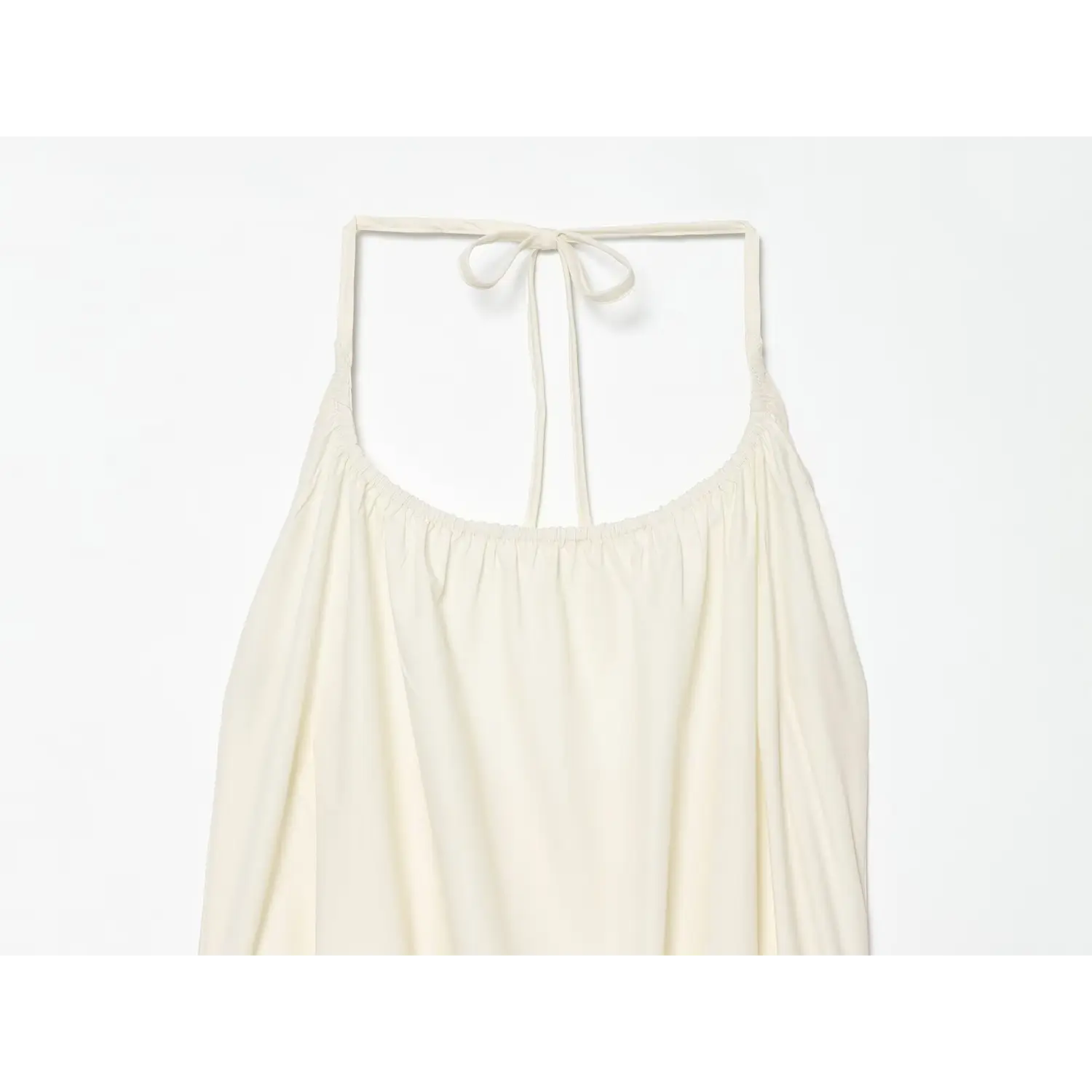 Close‑up of halter neckline, elastic gathered bust and halter tie straps on cream flowy mini dress