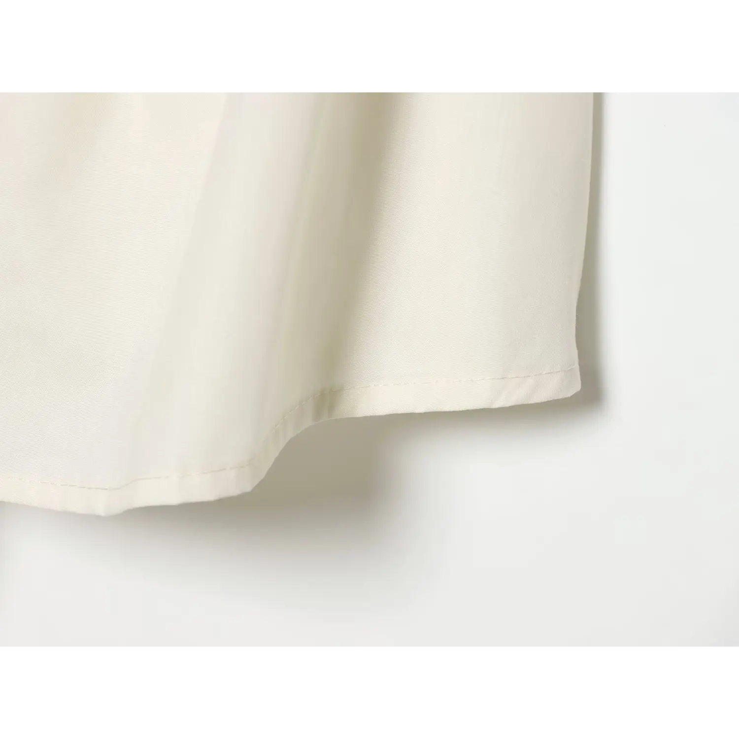 Extreme close‑up of finished hem stitching, smooth lightweight fabric texture of cream halter mini dress