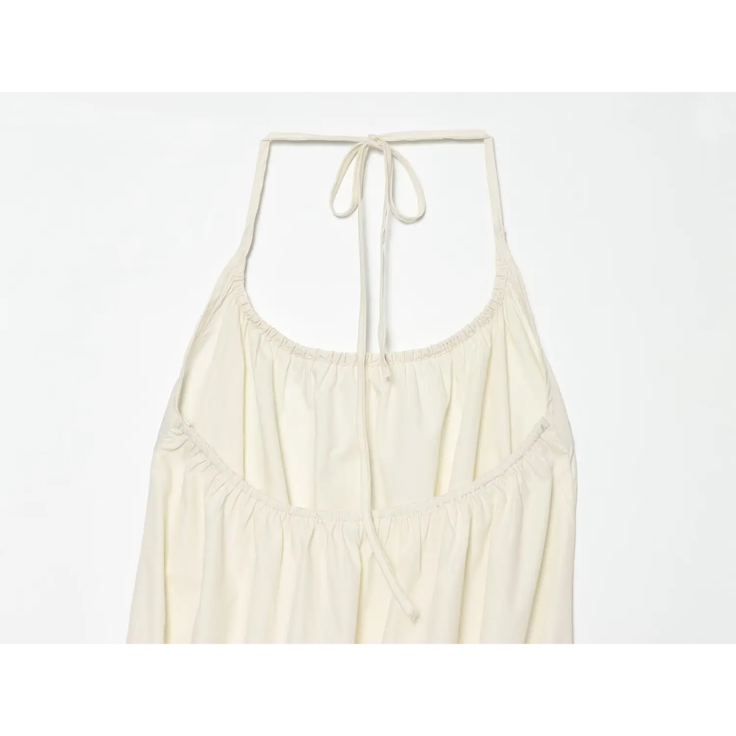 Flat close‑up of dress inner back, halter tie‑back straps, elastic gathered bust construction for cream tiered mini dress
