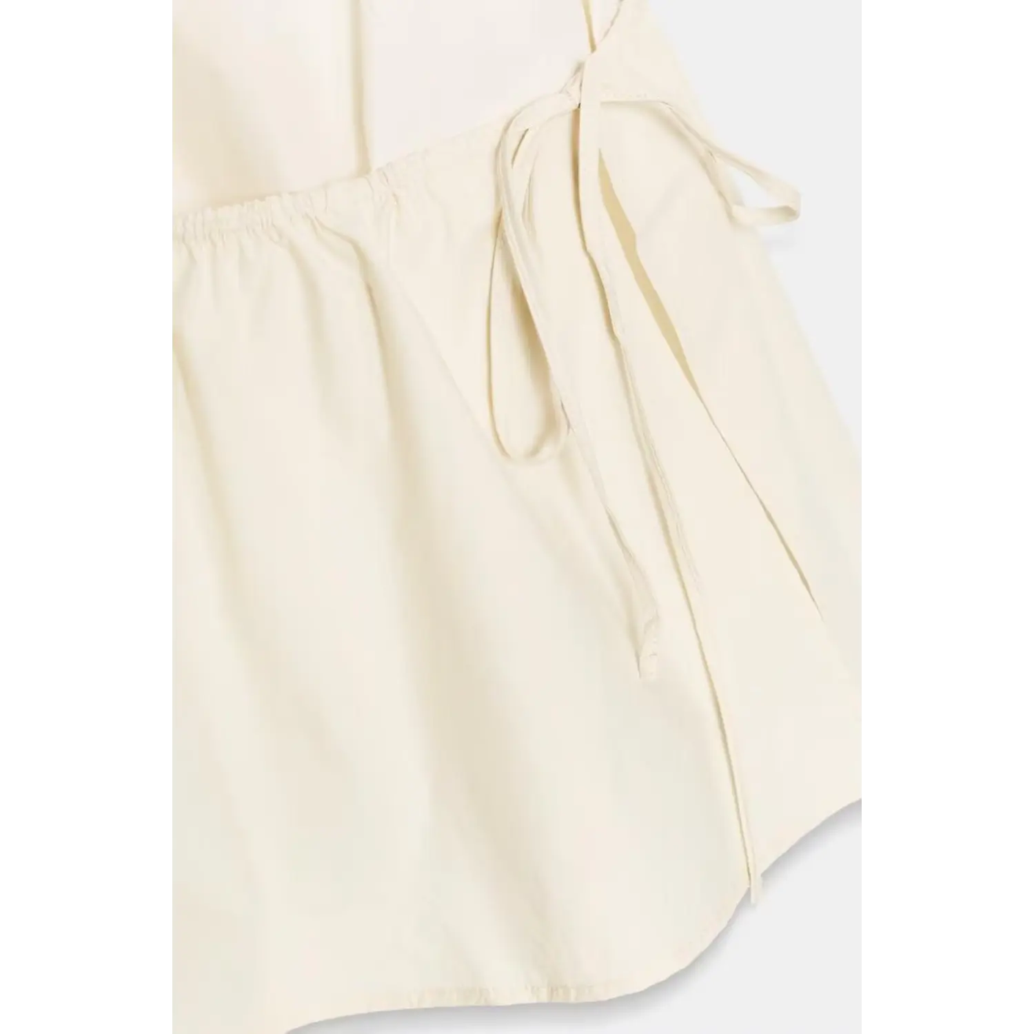Angled partial shot showing side drawstring tie, gathered waist and flowy ruffle skirt fabric of cream halter mini dress