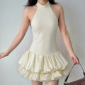 Model wearing a cream halter neck mini dress, showcasing the high neckline, fitted bodice, and double-layered ruffled skirt.