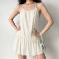 Model wearing cream halter tiered mini dress, front view, loose flowy silhouette, side waist drawstring tie, minimalist indoor studio setting