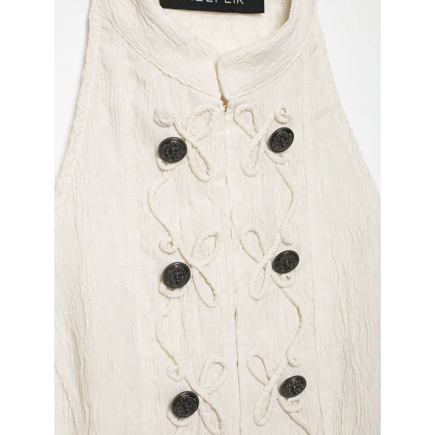 Extreme close‑up front decorative black buttons and rope embroidery on cream halter top