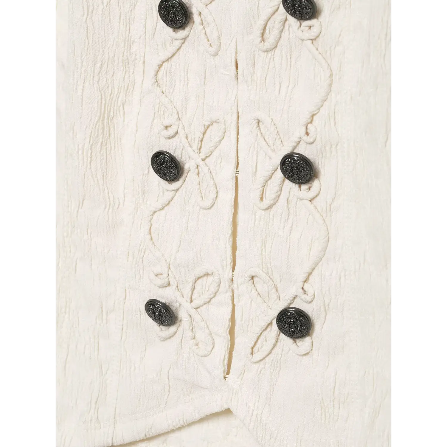 Close‑up of lower front decorative black buttons and rope embroidery on cream halter sleeveless top