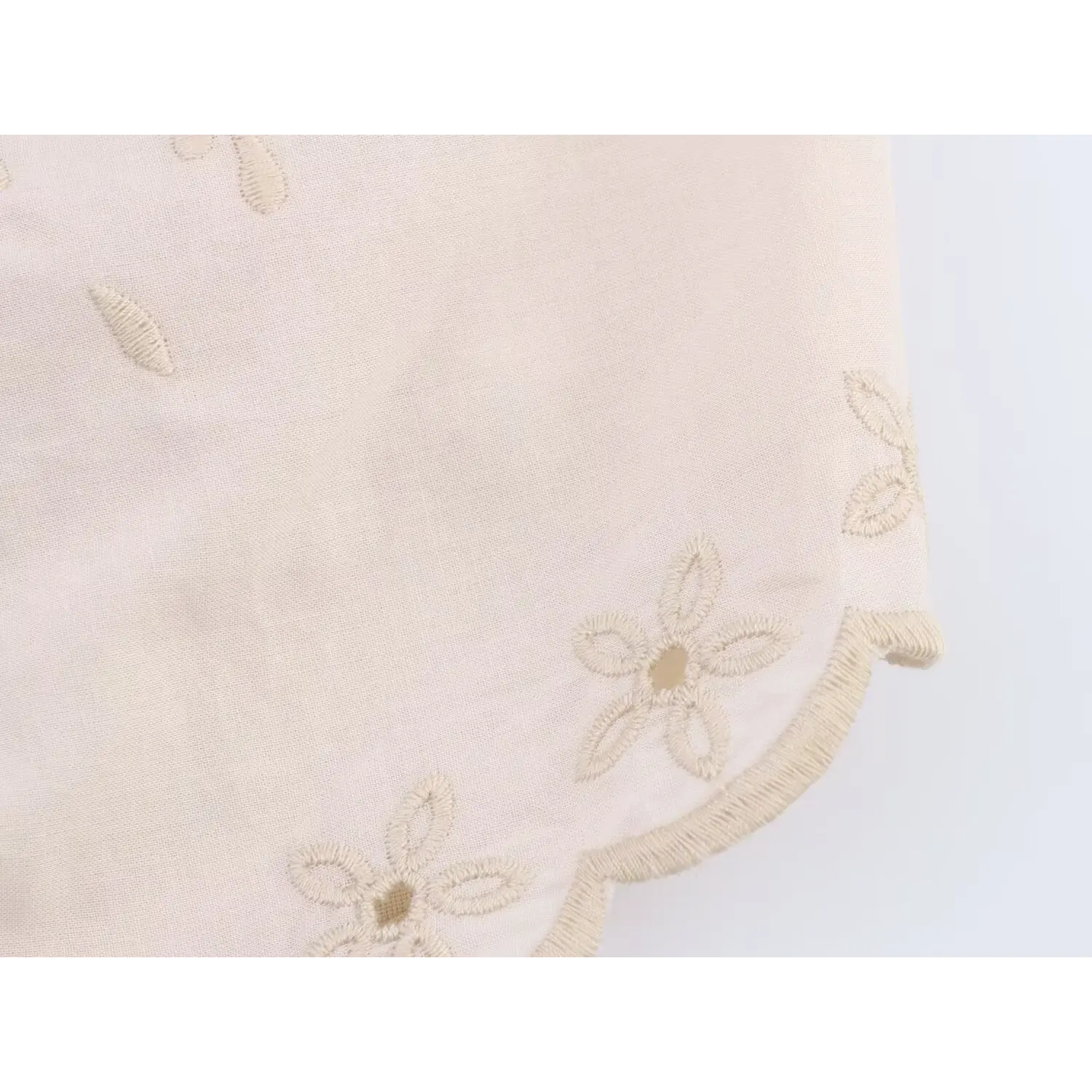 Close‑up of scalloped hem edge with small flower embroidery on cream halter crop top