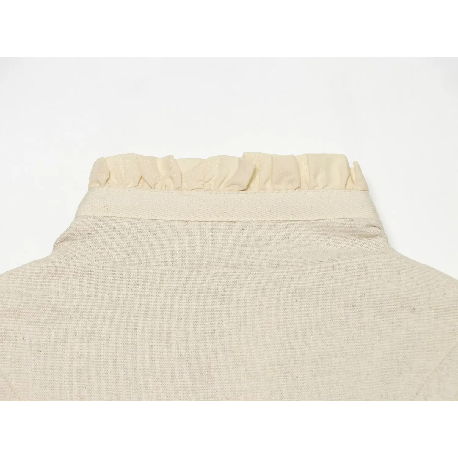 Close‑up of back neck ruffle trim and woven fabric texture of cream cropped jacket