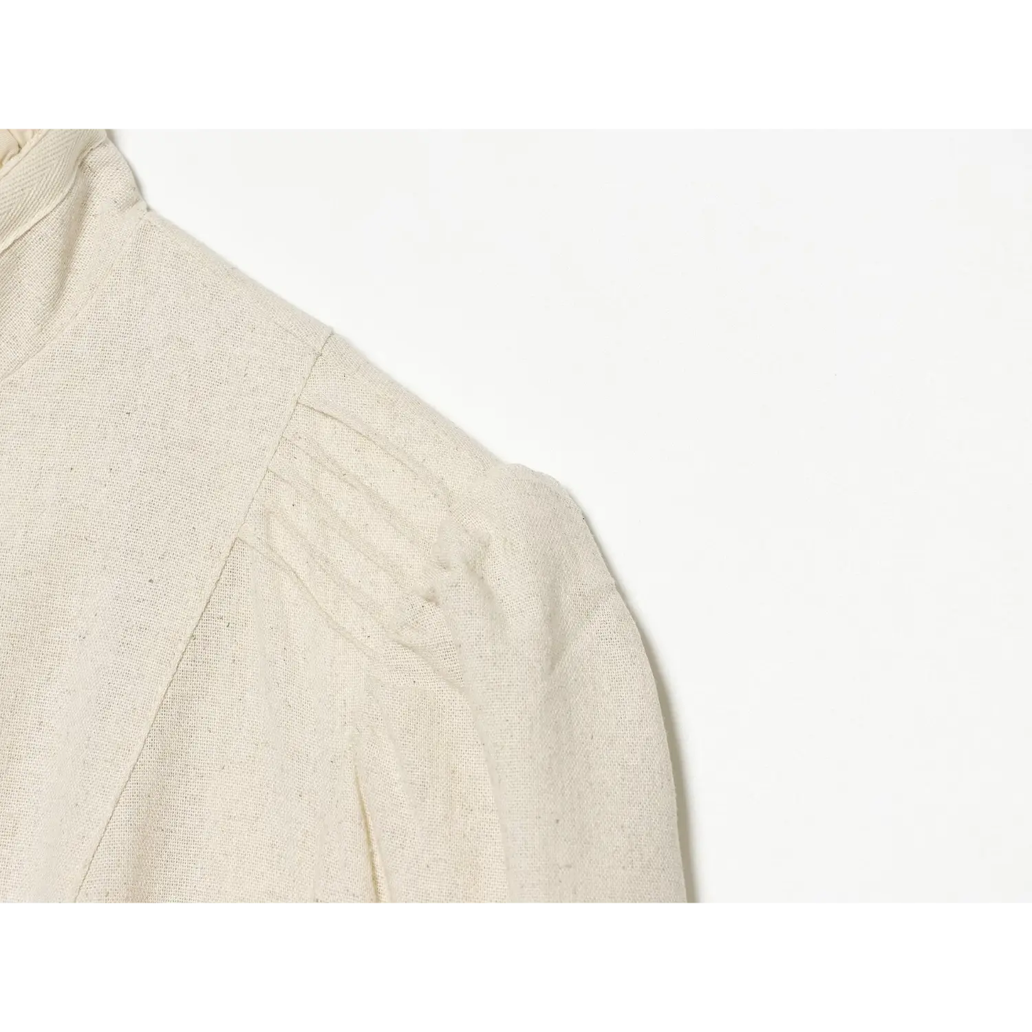 Close‑up of pleated puff shoulder seam detail on cream ruffle cropped jacket, linen blend texture