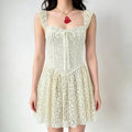 Model wearing a cream lace corset-style mini dress with ruffled straps, a front bow detail, and a flared skirt.