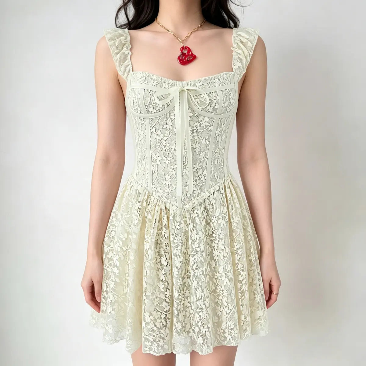 Model wearing a cream lace corset-style mini dress with ruffled straps, a front bow detail, and a flared skirt.