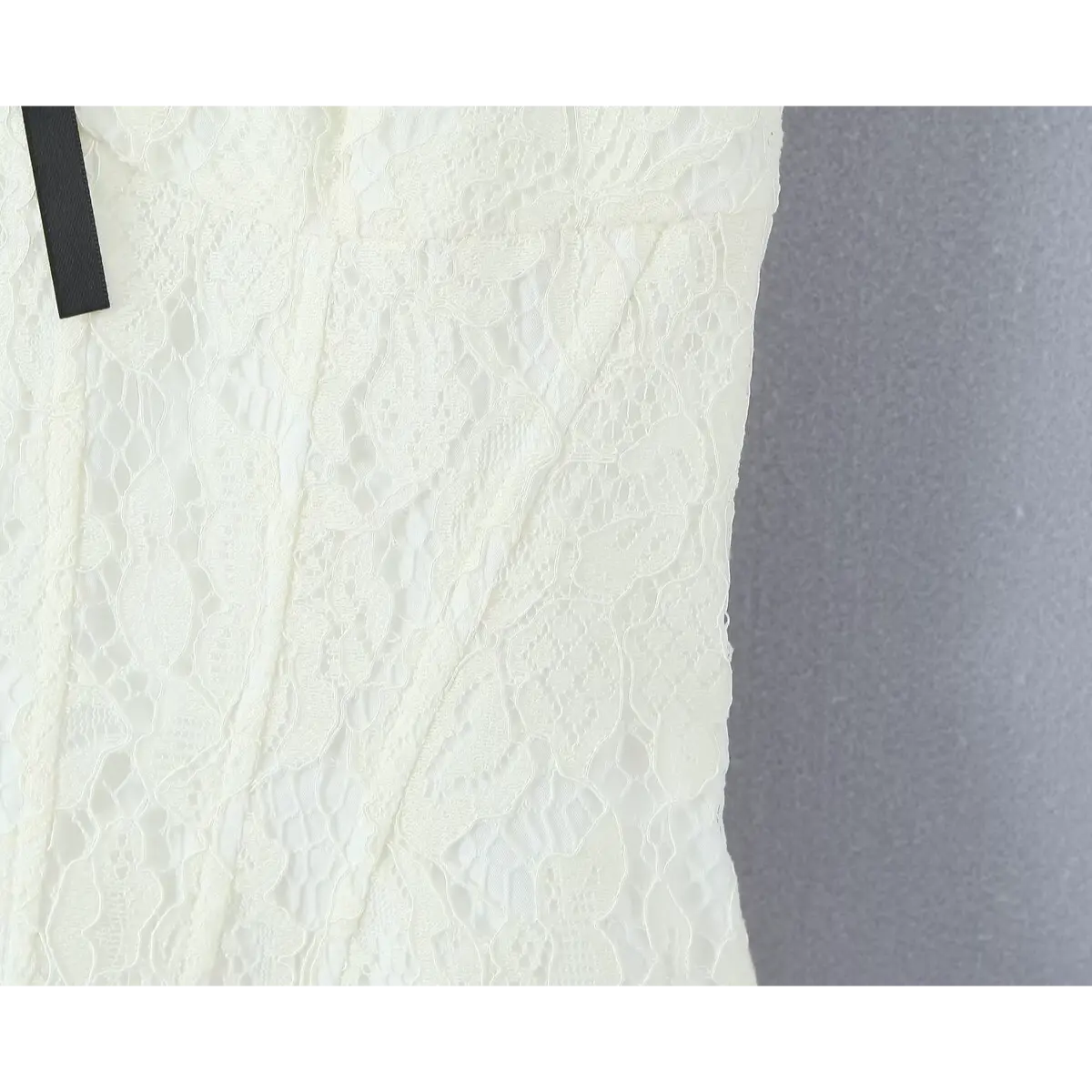 Close-up of the fitted lace bodice of a cream dress, highlighting the vertical seams and a small black ribbon accent.