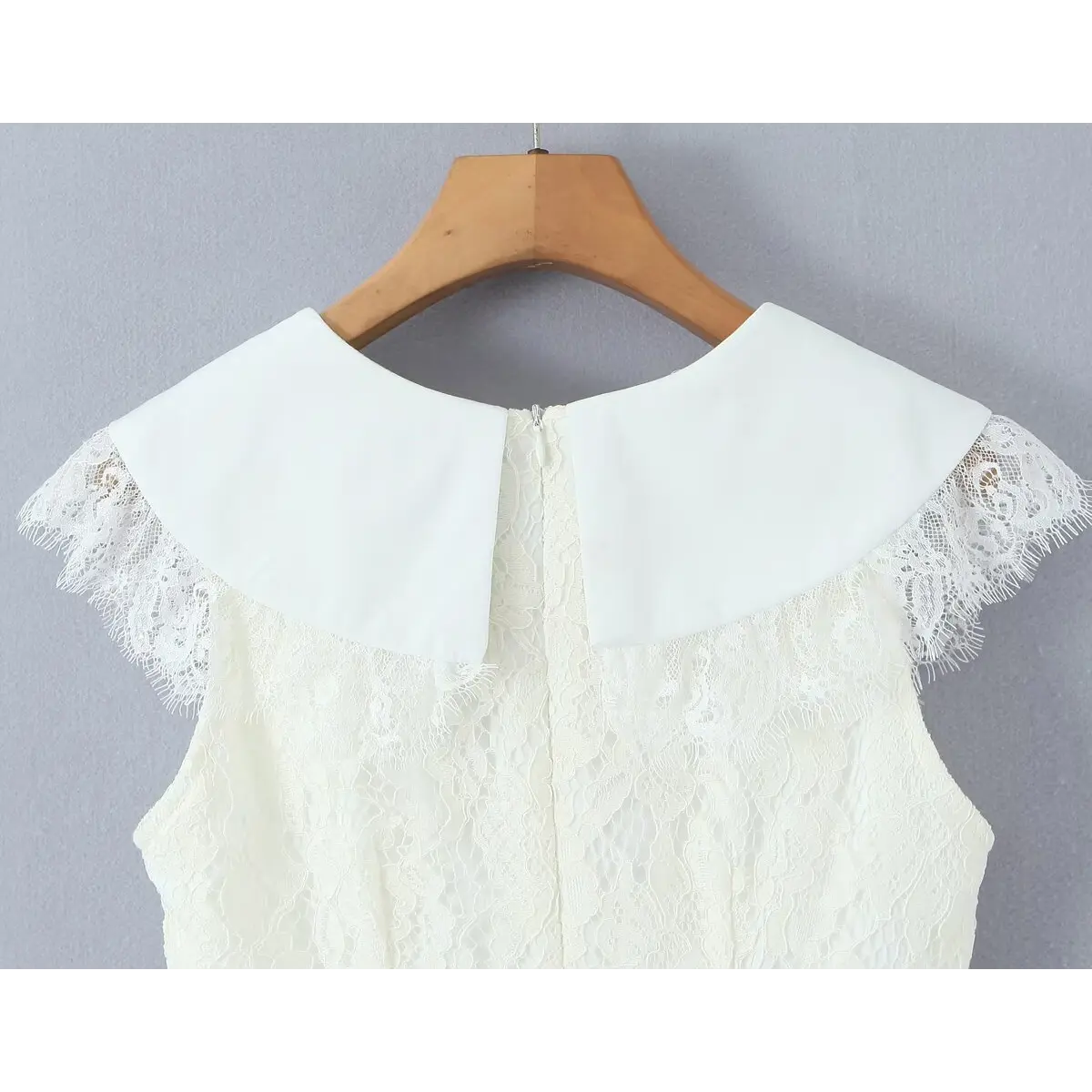 Back view of a cream lace dress on a wooden hanger, featuring a large flat collar, cap sleeves with frayed lace trim, and a center-back zipper.
