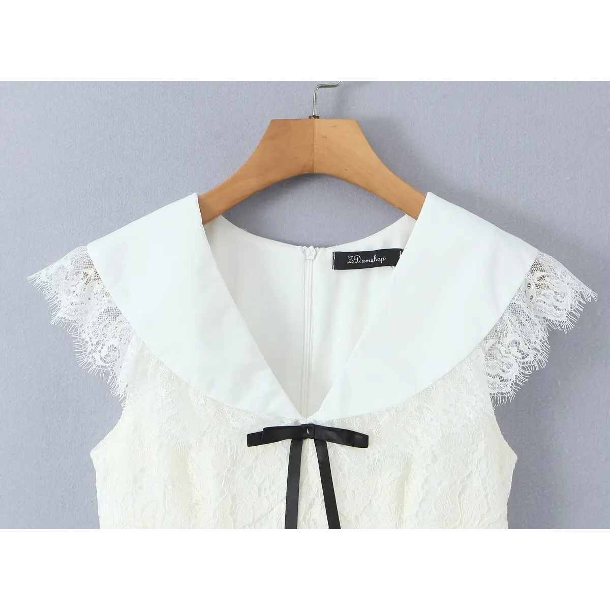 Front view of a cream lace dress on a wooden hanger, showing the large flat collar, black ribbon bow, and center-back zipper.