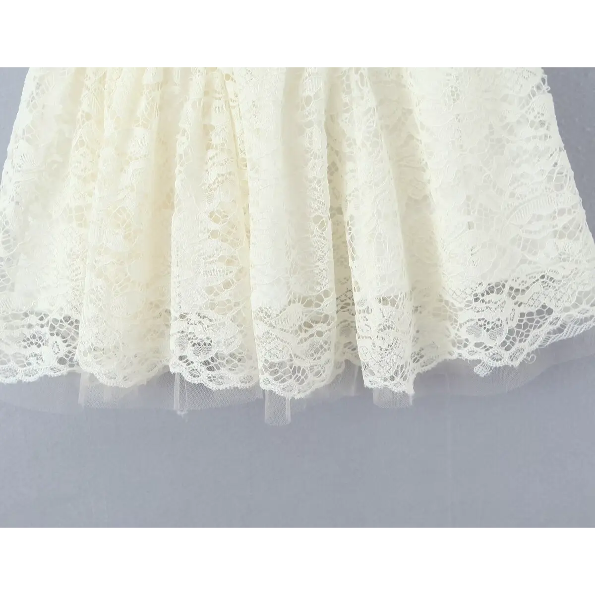 Close-up of the flared skirt hem on a cream lace dress, showing the gathered lace layers and sheer tulle trim.