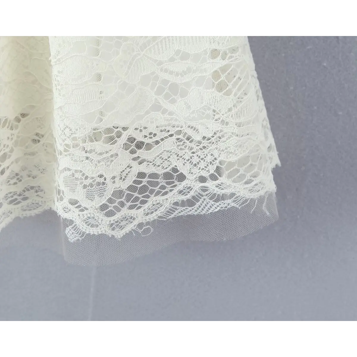 Close-up view of the scalloped lace hem on a cream-colored dress, showing the intricate floral pattern and sheer tulle underlayer.