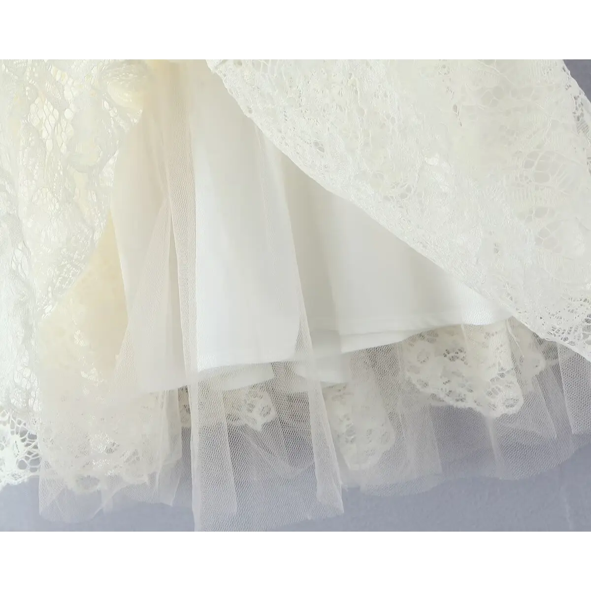 Close-up of the layered skirt of a cream lace dress, showing the lace overlay, smooth fabric lining, and sheer tulle underskirt.