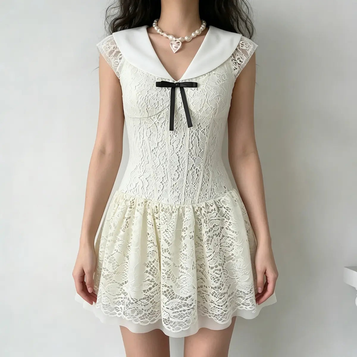 Model wearing a cream lace mini dress with a large flat collar, cap sleeves, and a black ribbon bow, holding a small wicker bag and wearing a pearl necklace.