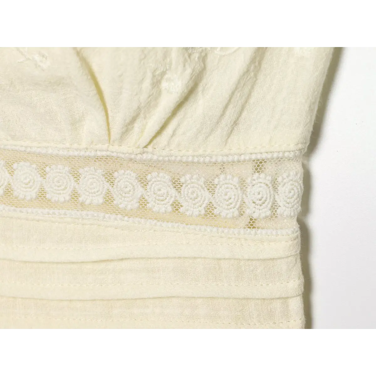 Close-up of the waist on the cream bustier top, showing the floral lace inset, embroidered fabric, and pleated waistband