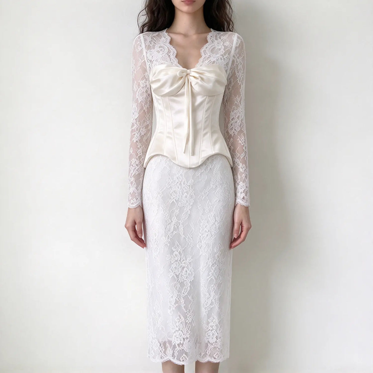 Model wearing cream long sleeve lace maxi dress, v-neck sheer floral lace sleeves, large front bow corset top, fitted lace skirt, plain white background