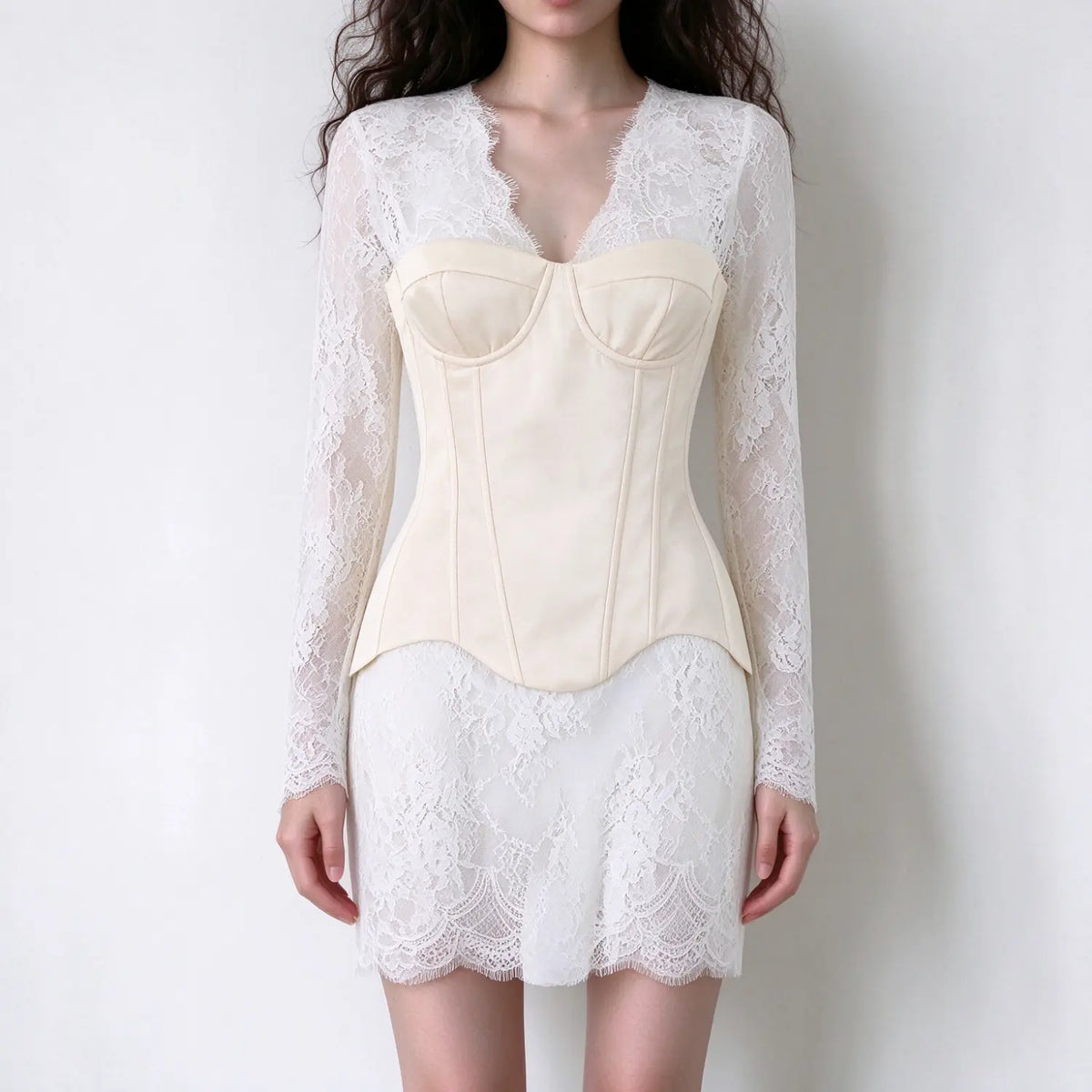 Model wearing cream lace long sleeve mini dress, v-neck sheer lace sleeves, fitted corset top, delicate floral lace skirt, white backdrop
