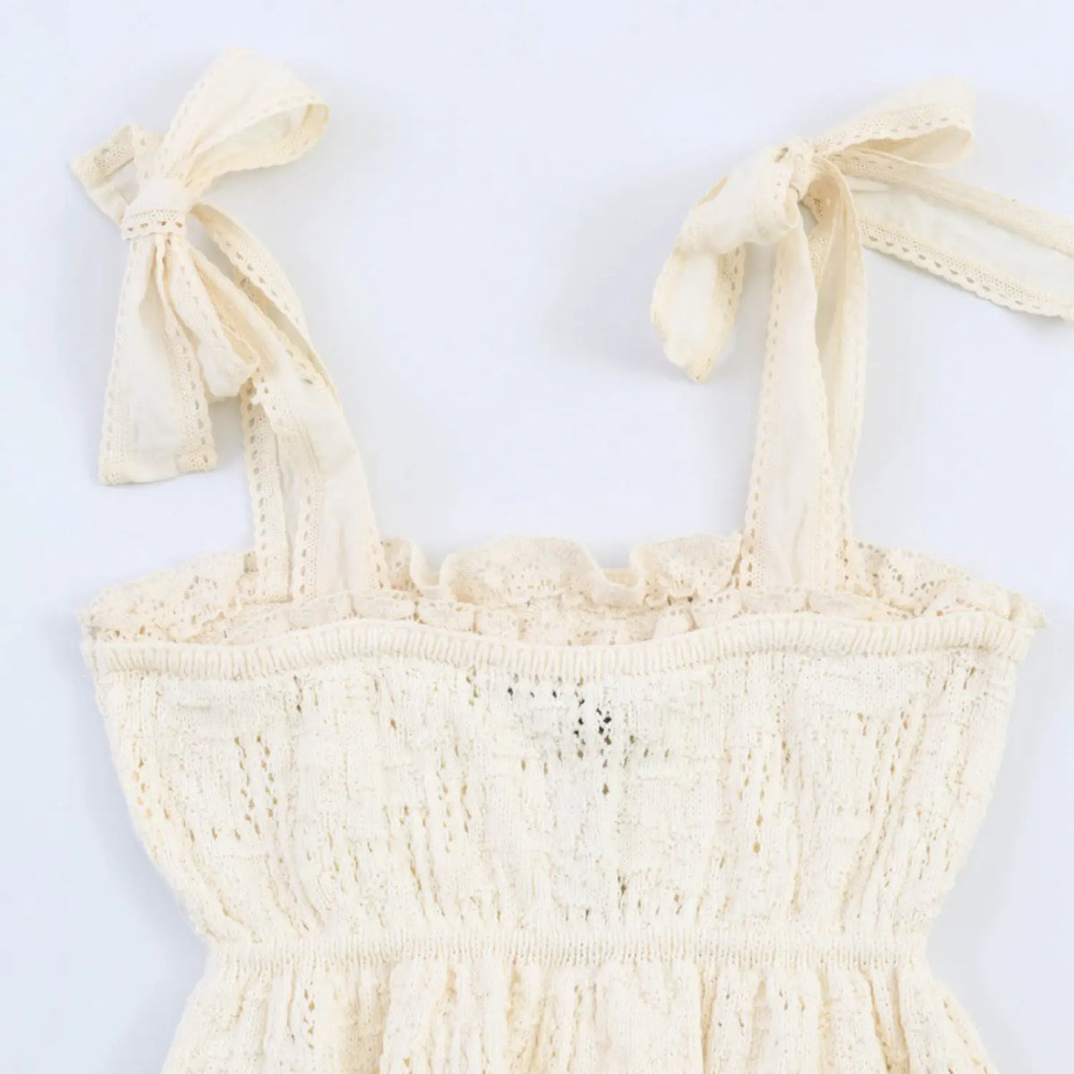 Close‑up bodice shot cream lace camisole top with self‑tie bow straps smocked lace ruffle neckline detail