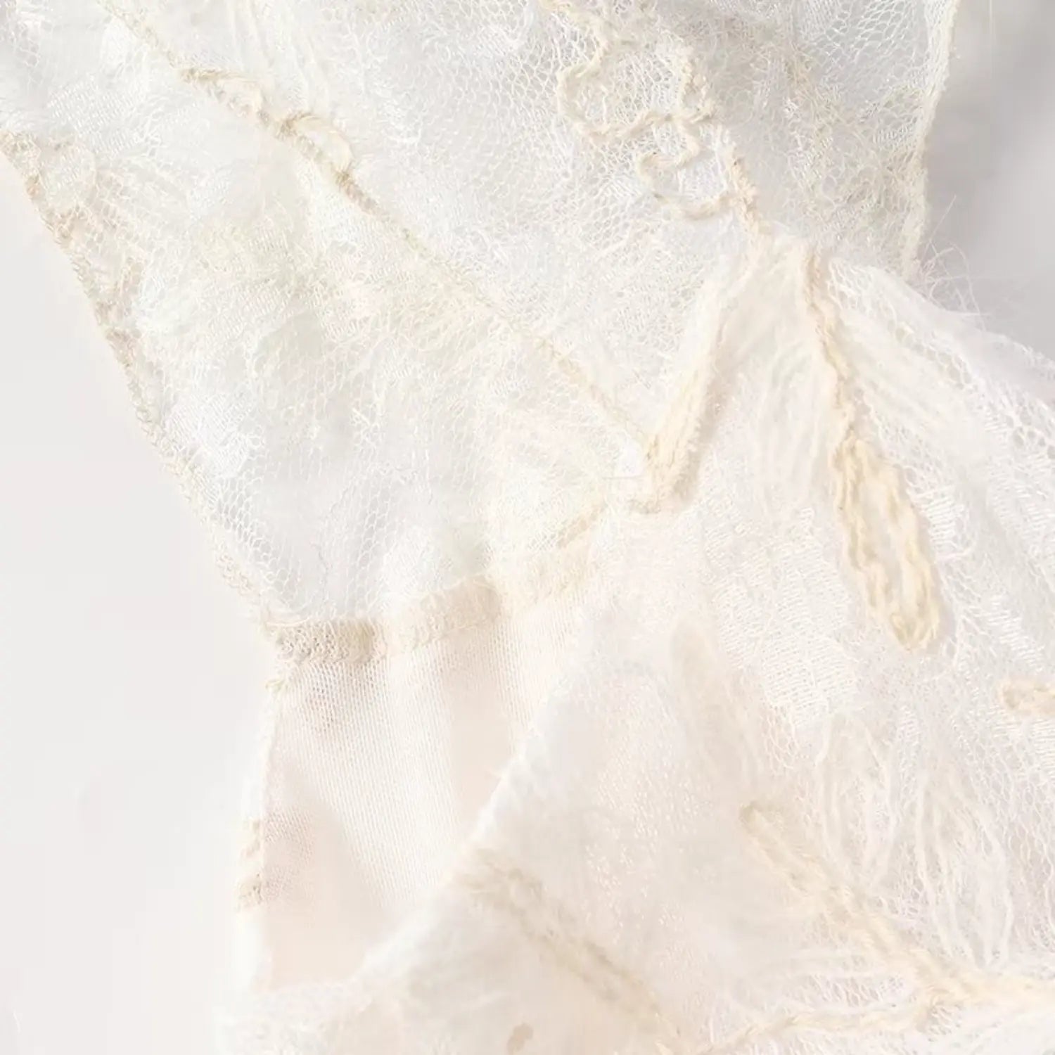 Close-up of floral feather embroidery on sheer cream lace fabric with subtle fuzzy texture
