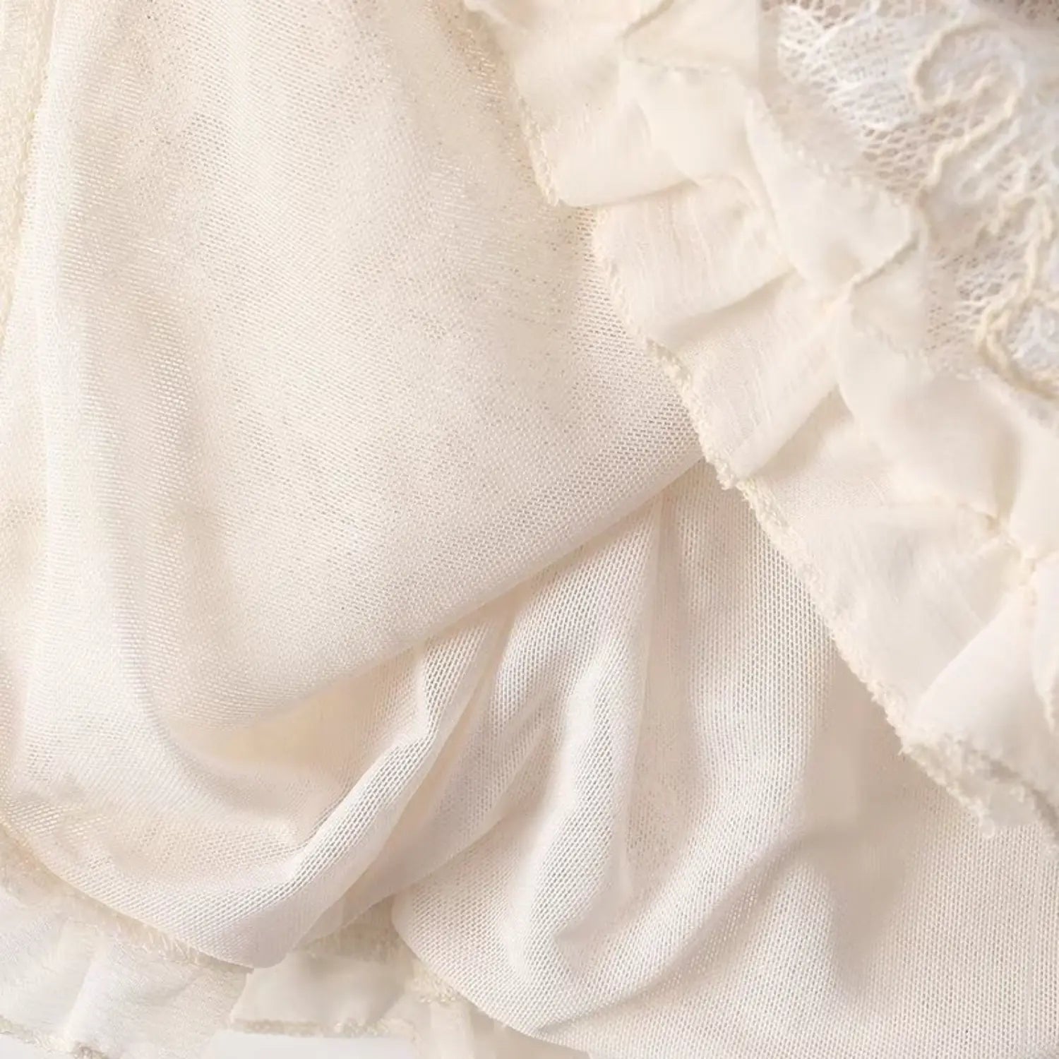 Close view of soft mesh inner lining and ruffle hem construction of cream lace sleeveless blouse