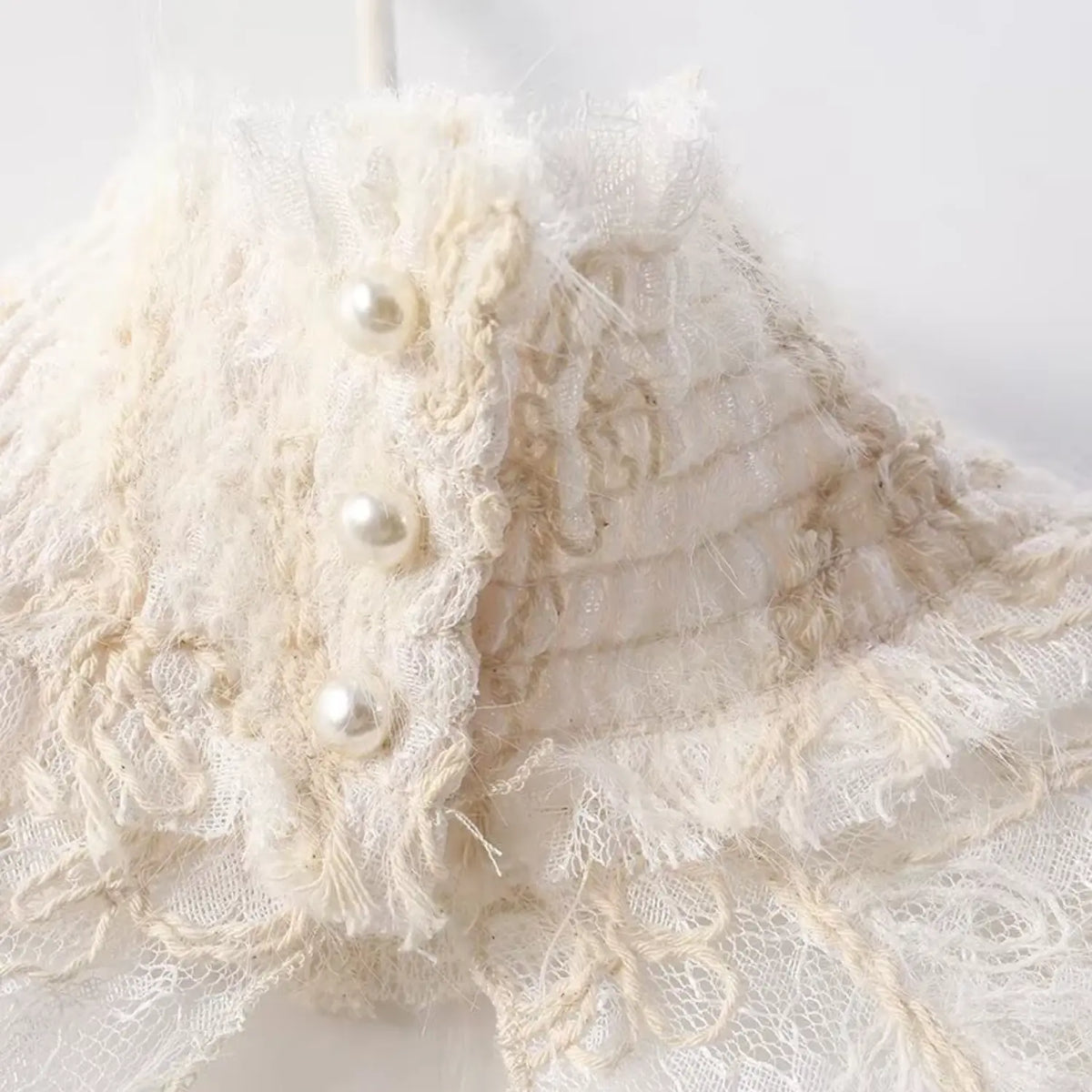 Close-up of high ruffled neck with pearl buttons on cream floral lace sleeveless top