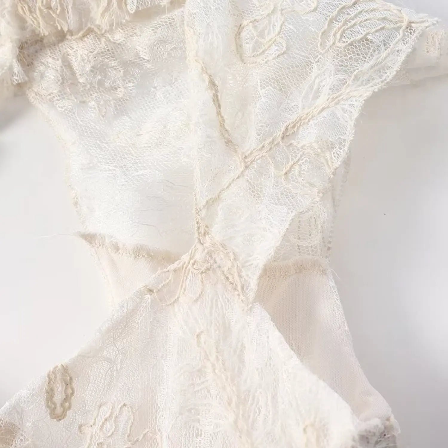 Macro shot of floral embroidery and cap sleeve ruffle detail on cream lace top