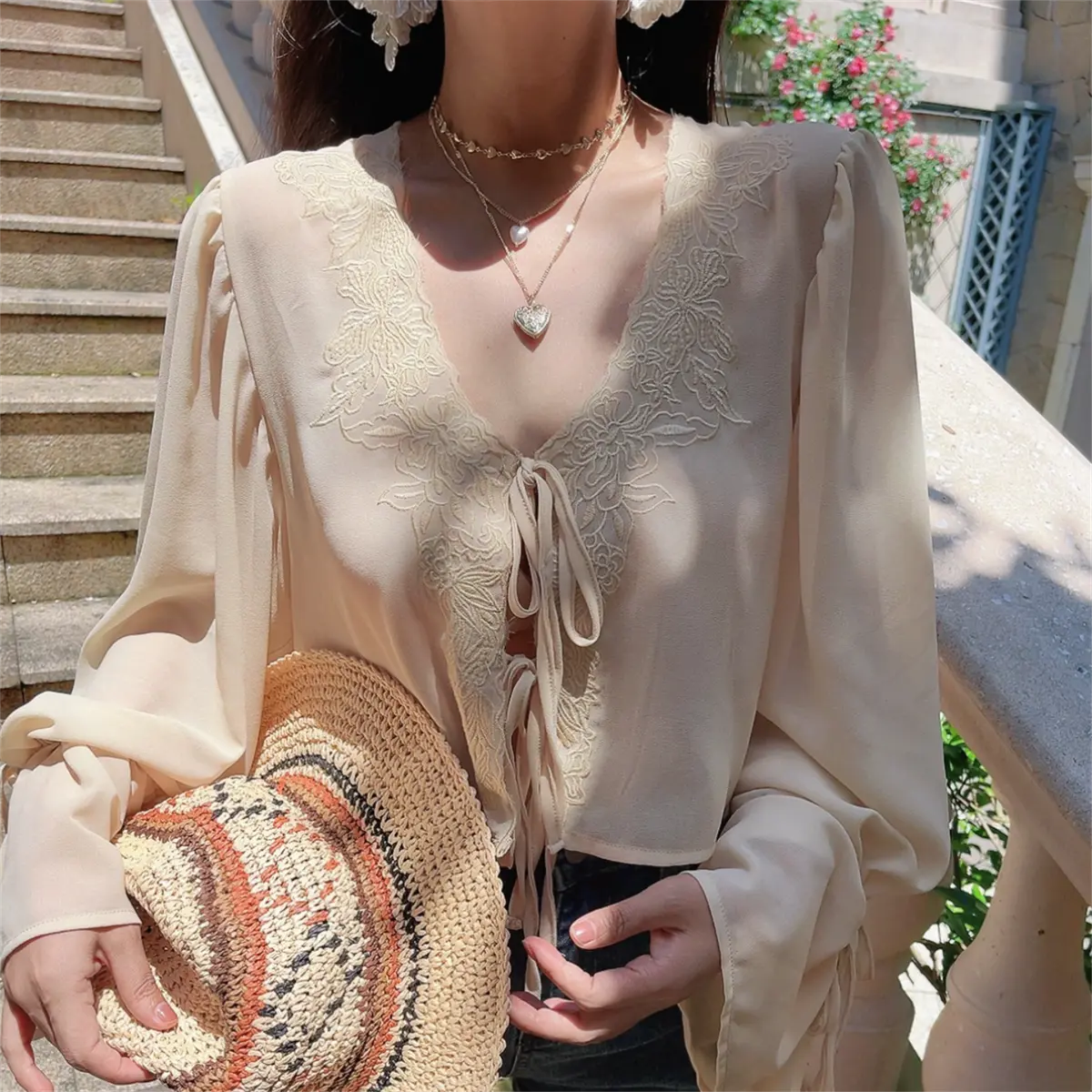  Front view of a model in a cream lace-trim chiffon blouse, featuring floral embroidery and bell sleeves.
