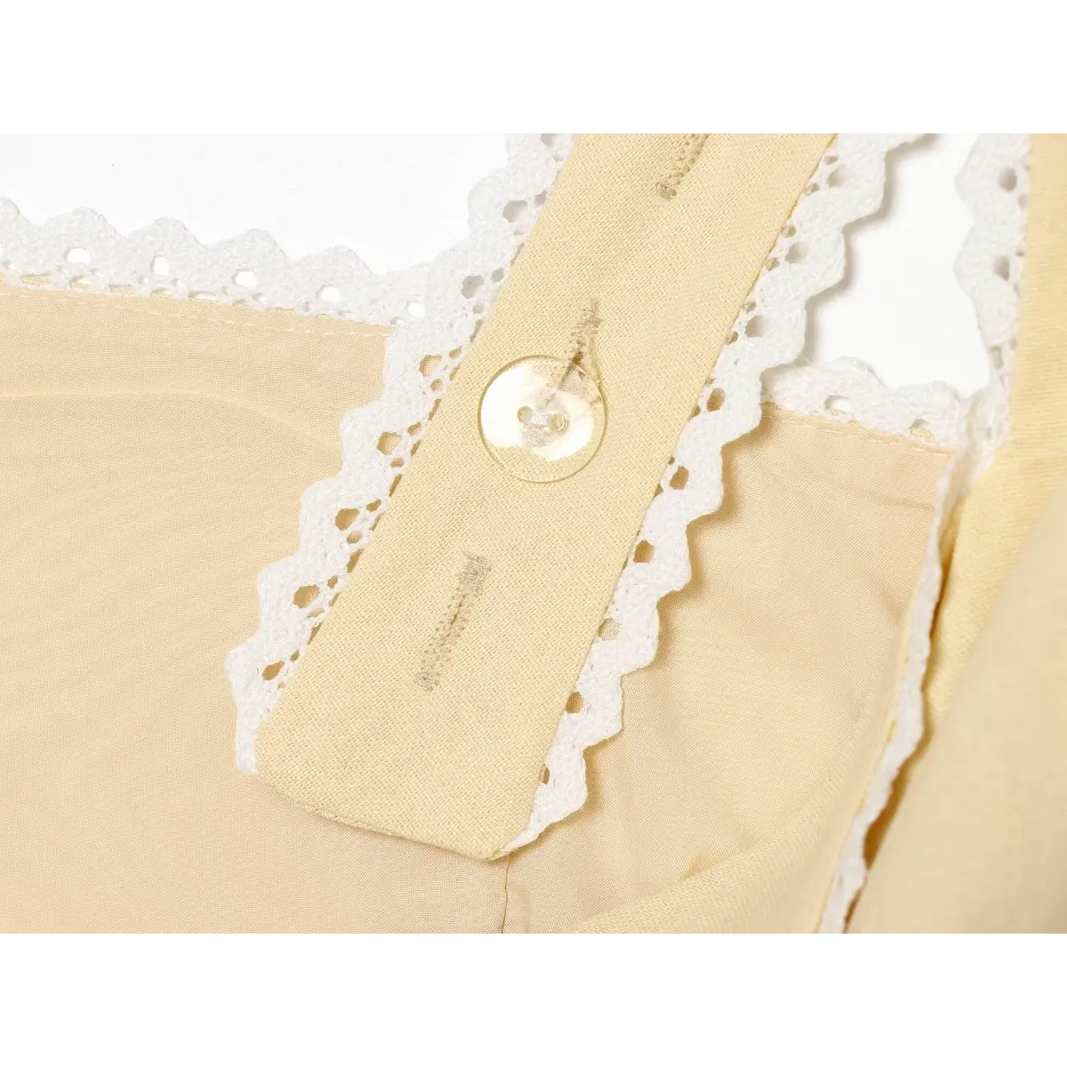 Close-up of the transparent button on the strap of a cream-colored lace-trimmed top.