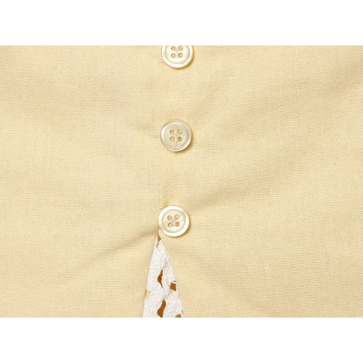 Close-up of the front buttons and lace-trimmed hem on a cream-colored top.