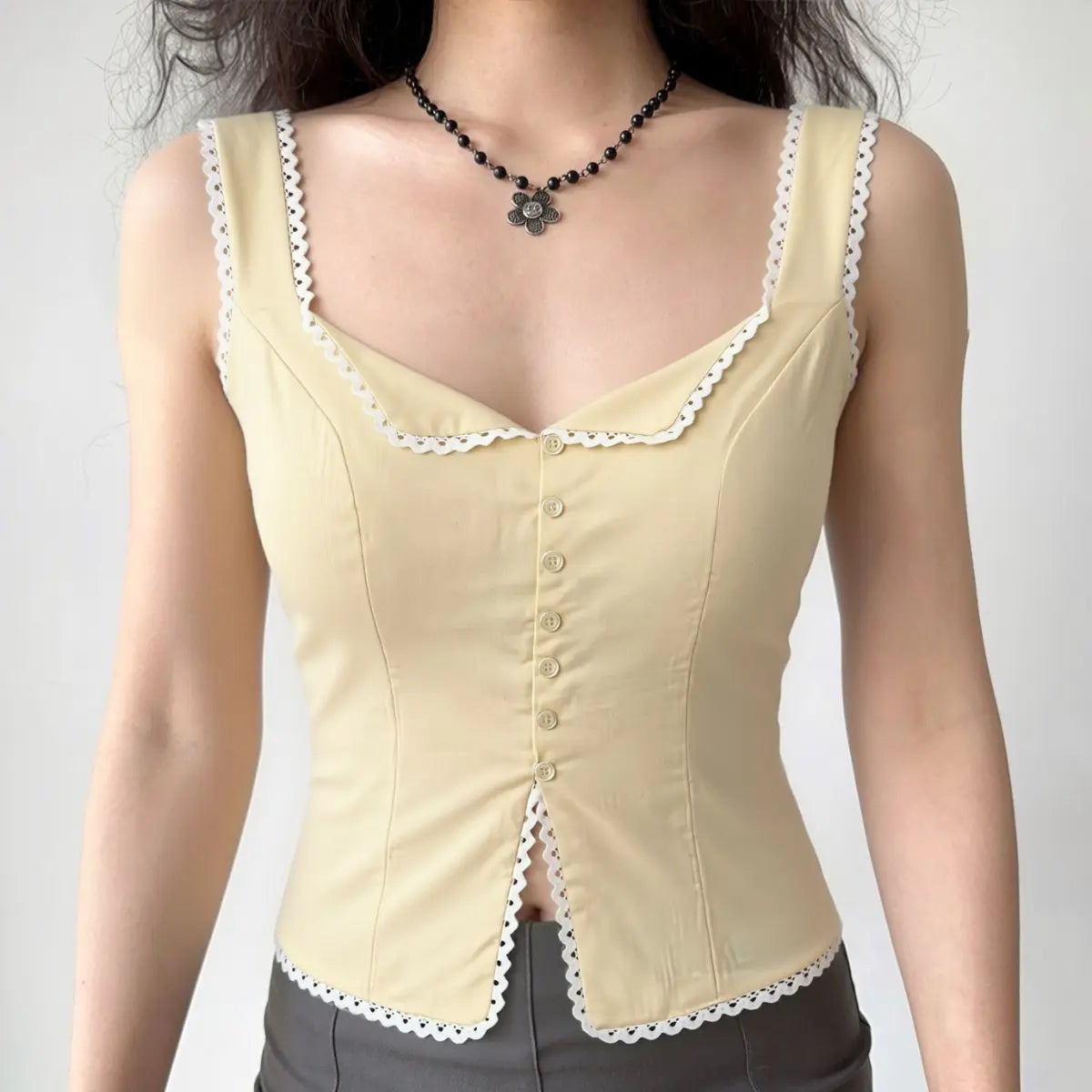 Full-body shot of a woman wearing a cream-colored lace-trimmed corset-style top with gray bottoms.