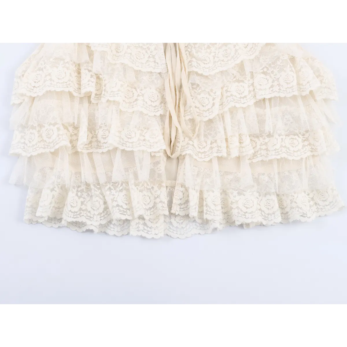 Close-up detail of the layered floral lace and tulle ruffles on a cream camisole, showing the intricate rose pattern and scalloped edges.