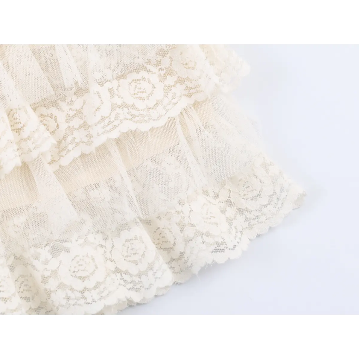 Close-up detail of the scalloped lace hem and ruffled layers on a cream camisole, showing the sheer tulle and floral pattern.