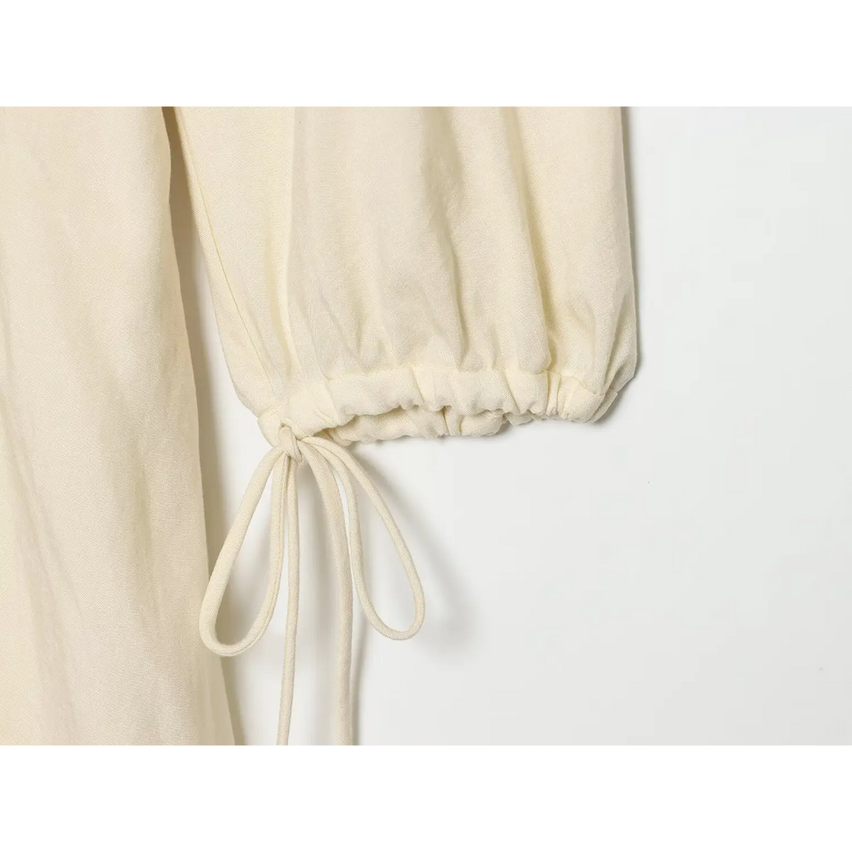 Close‑up of balloon sleeve cuff with self‑fabric drawstring tie on cream linen dress