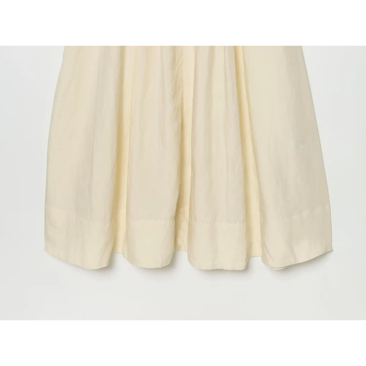 Close‑up of pleated flowy skirt and finished hem of cream linen maxi dress