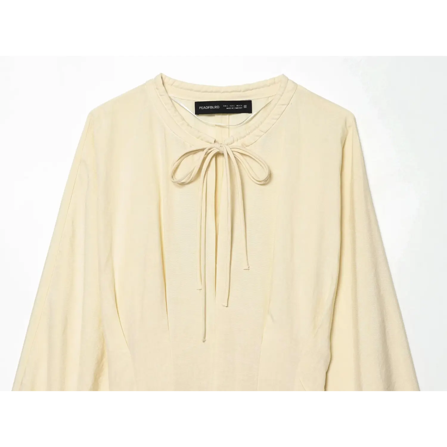 Close‑up of cream maxi dress neckline with front self‑fabric tie knot and inner clothing label