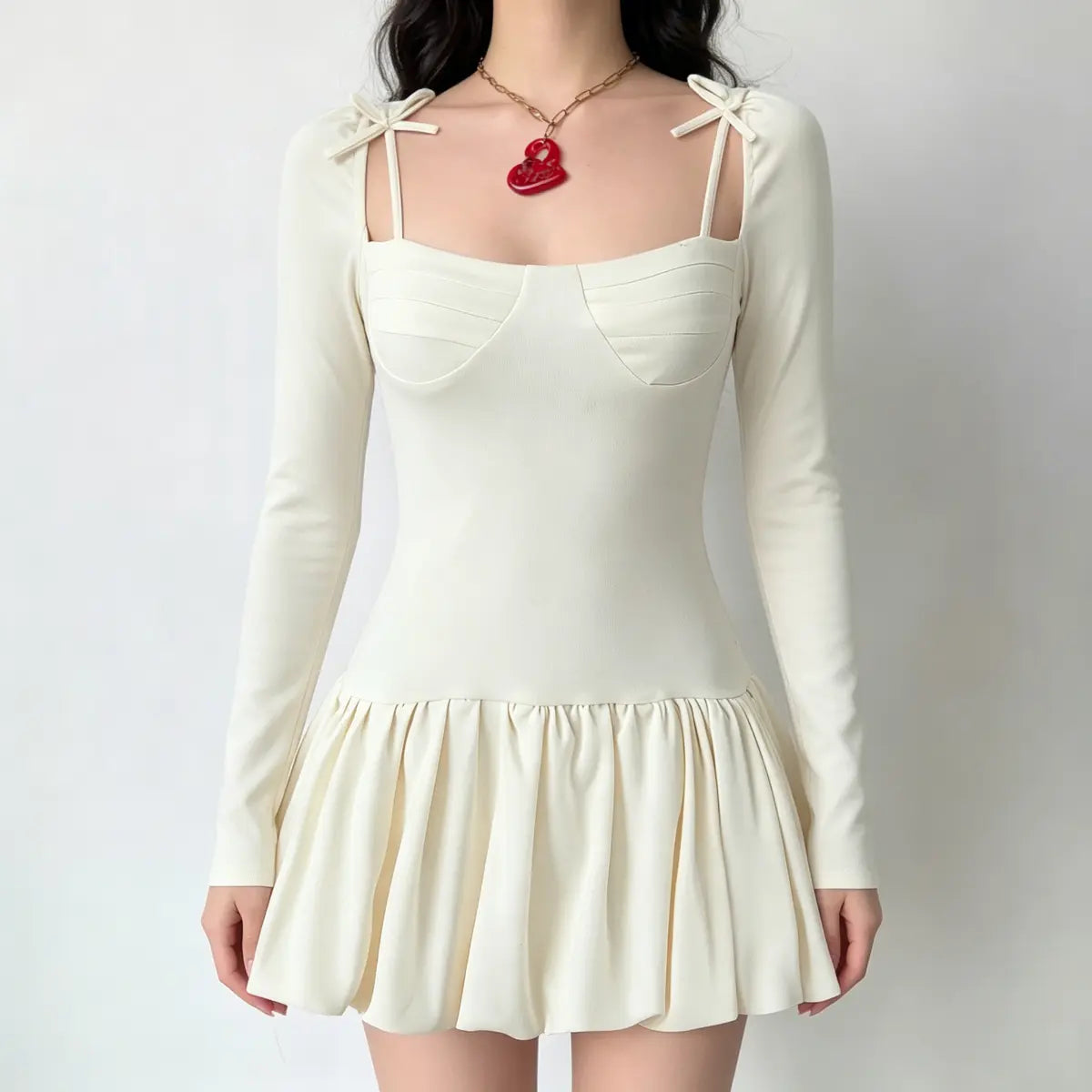  Model wearing a cream long-sleeve mini dress with a corset-style bust, shoulder bows, and a gathered flared skirt.