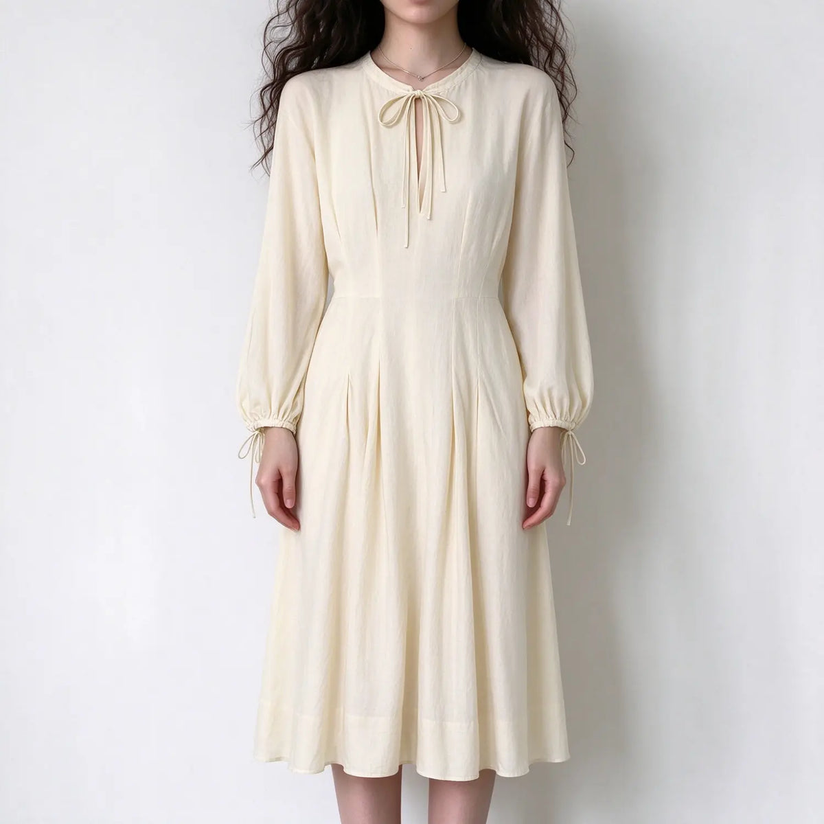 Model wearing cream long sleeve tie neck linen maxi dress with balloon sleeves and pleated skirt, white background