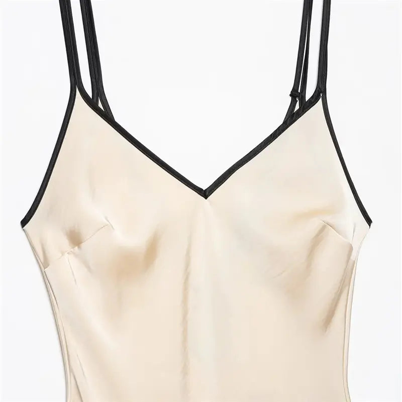 Closeup of solid style V neckline, black contrast piping edging, fixed bust dart shaping, double thin spaghetti straps with adjust slider, smooth cream satin texture