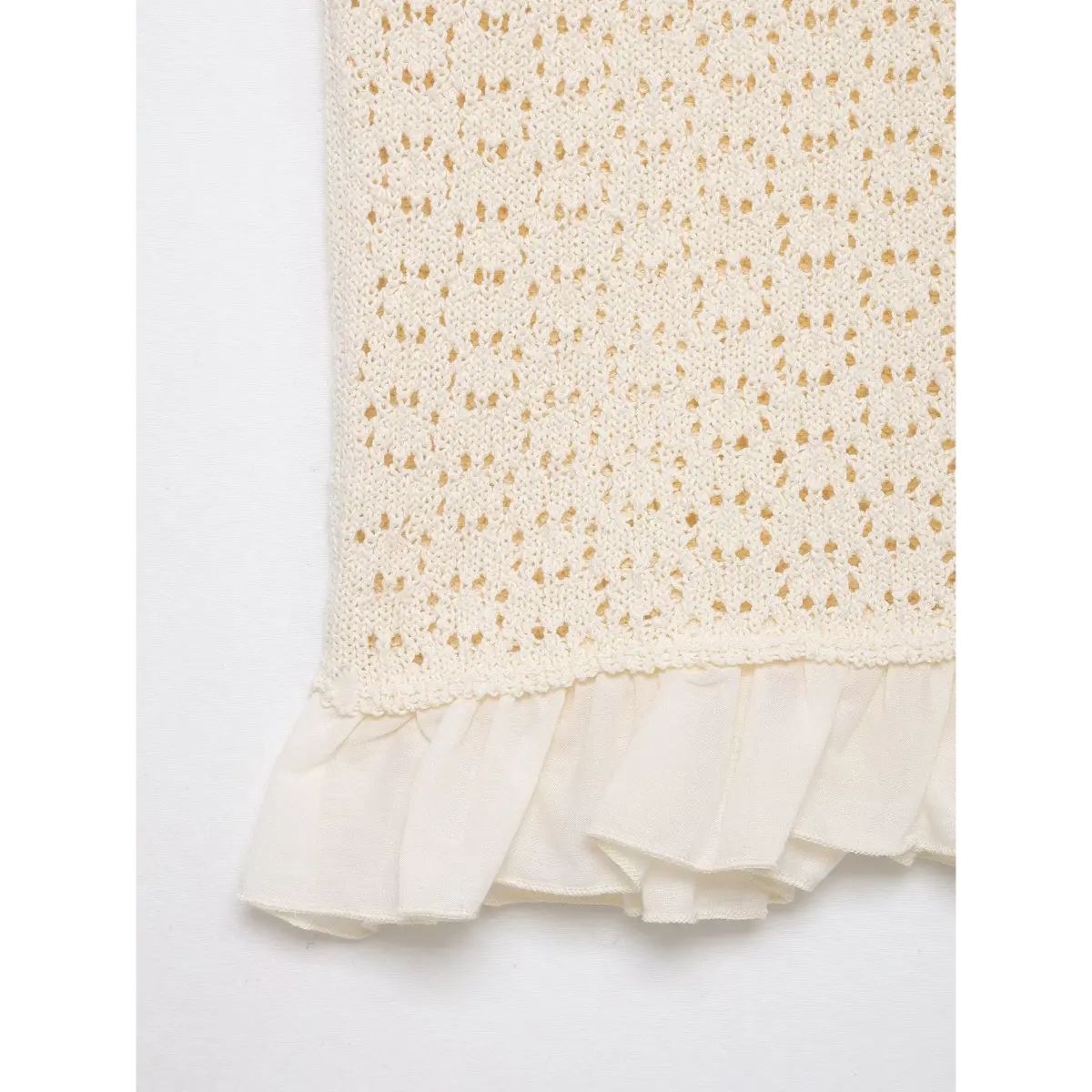 Close-up of the ruffled hem on the cream openwork knit top