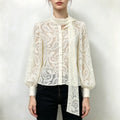 Model wearing cream paisley lace pussy bow button blouse with black jeans, front view