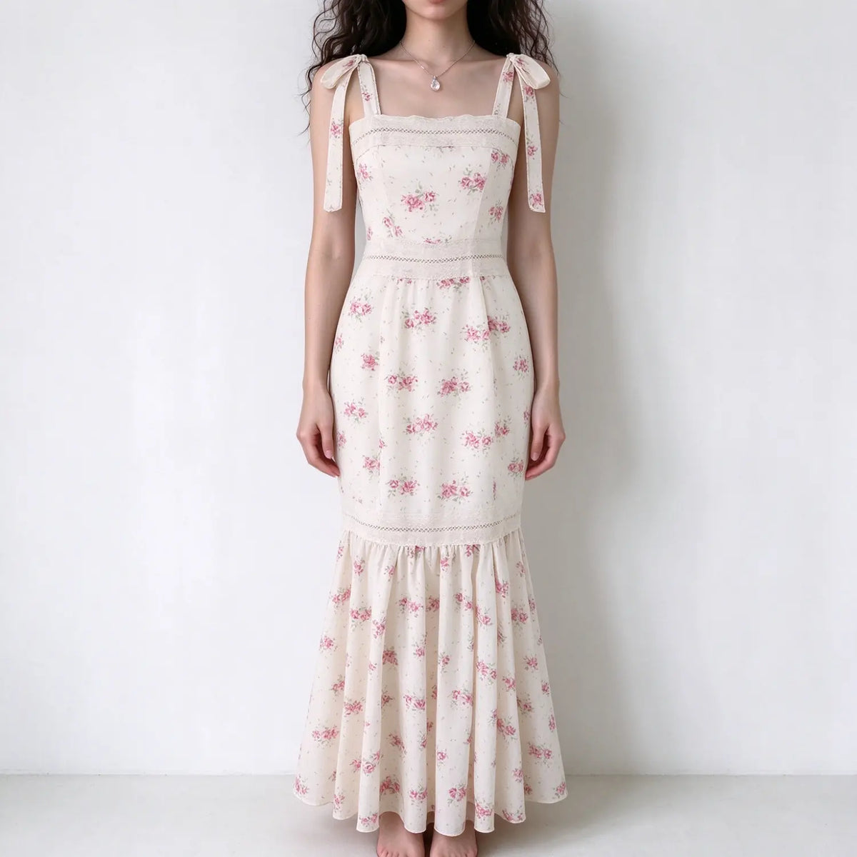 Model wearing cream pink floral maxi dress, square neck, tie bow shoulder straps, lace trim, mermaid ruffle hem, plain white background